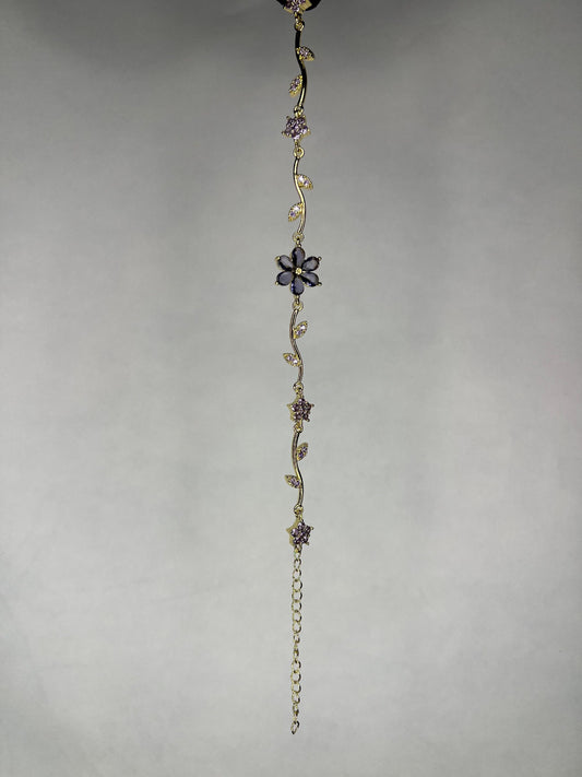Close-up image of gold-plated flower vine bracelet with purple amethyst gems on a plain background