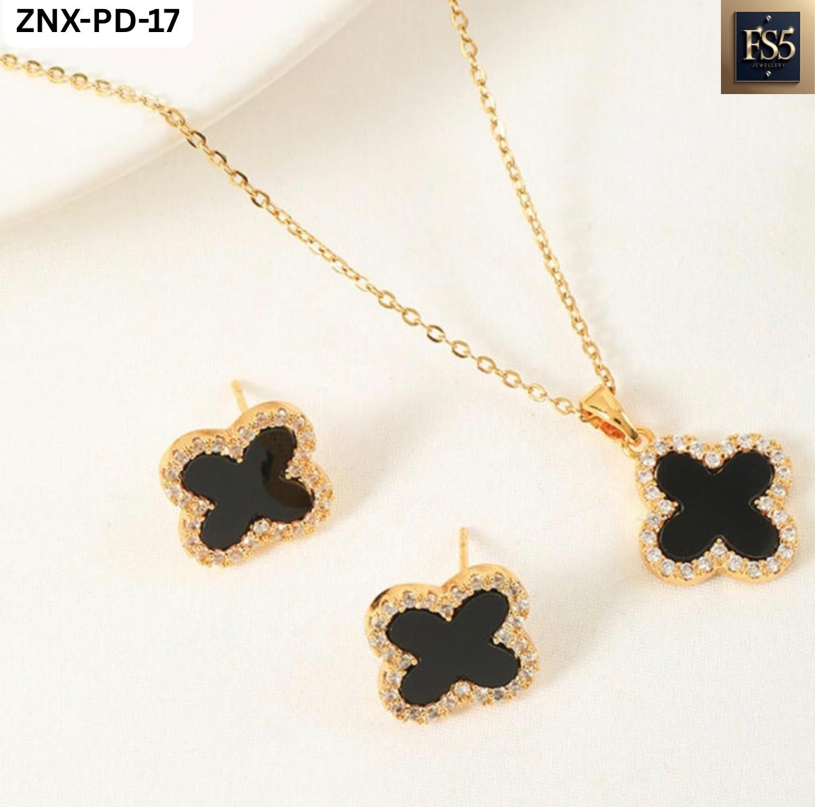Necklace and earrings laid out showing black clover centers bordered by sparkling stones on gold-tone metal