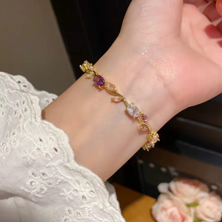 Gold bracelet with secure clasp and floral gemstone arrangement on plain white surface
