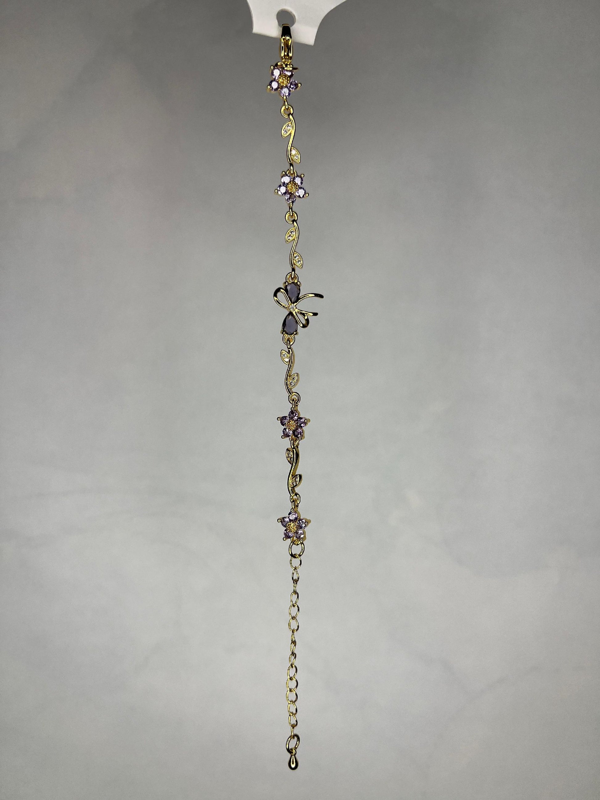 Close-up view of gold bracelet with floral and butterfly designs against a gray background