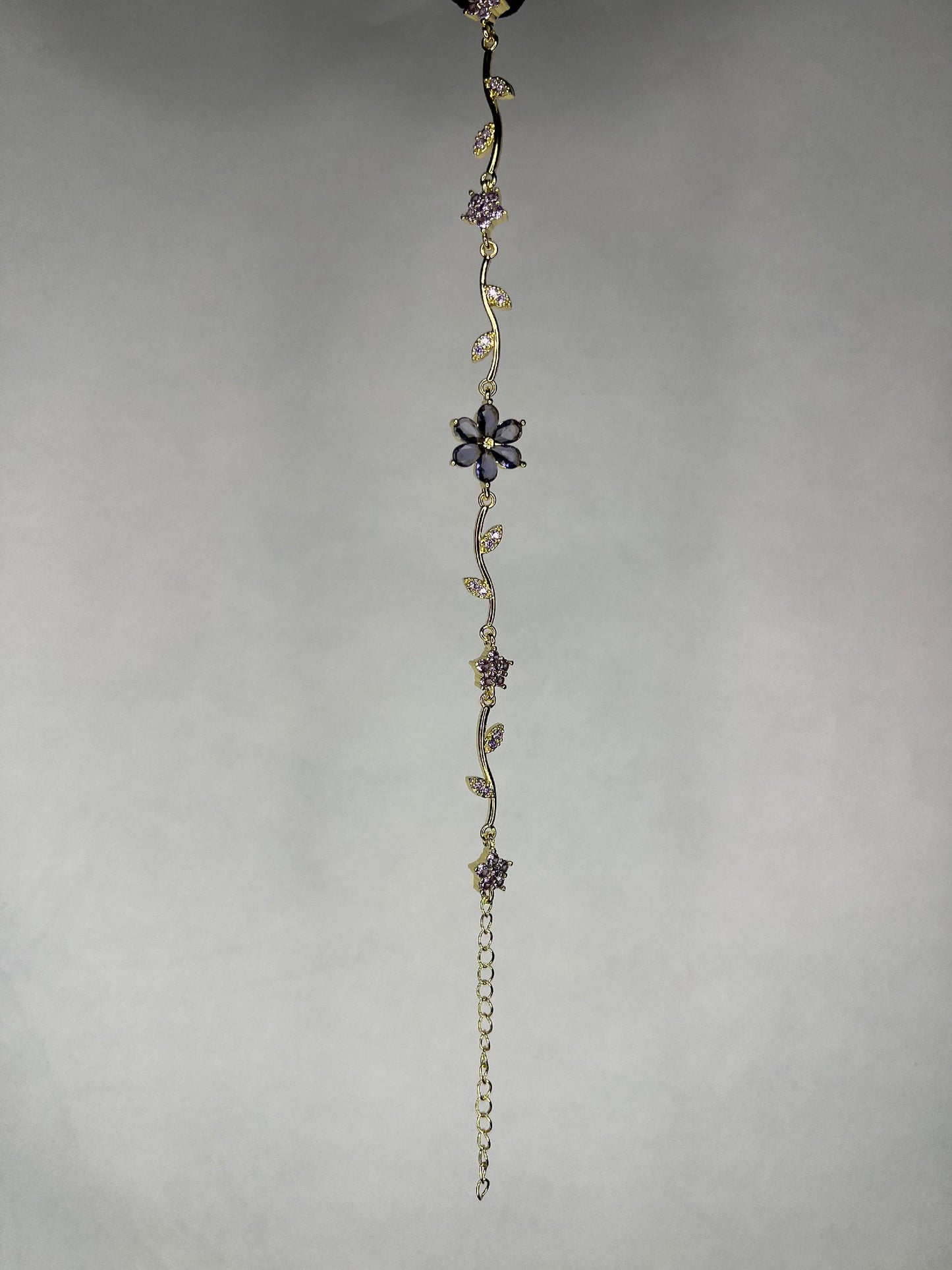 Close-up image of gold-plated flower vine bracelet with purple amethyst gems on a plain background