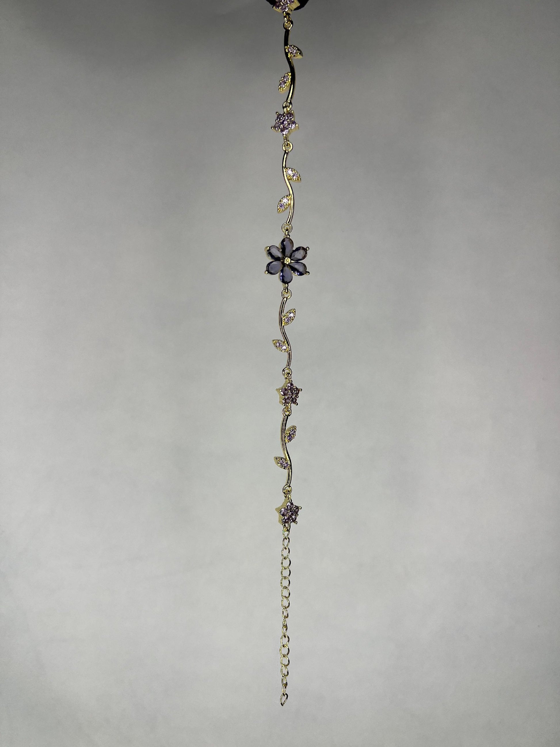 Close-up image of gold-plated flower vine bracelet with purple amethyst gems on a plain background