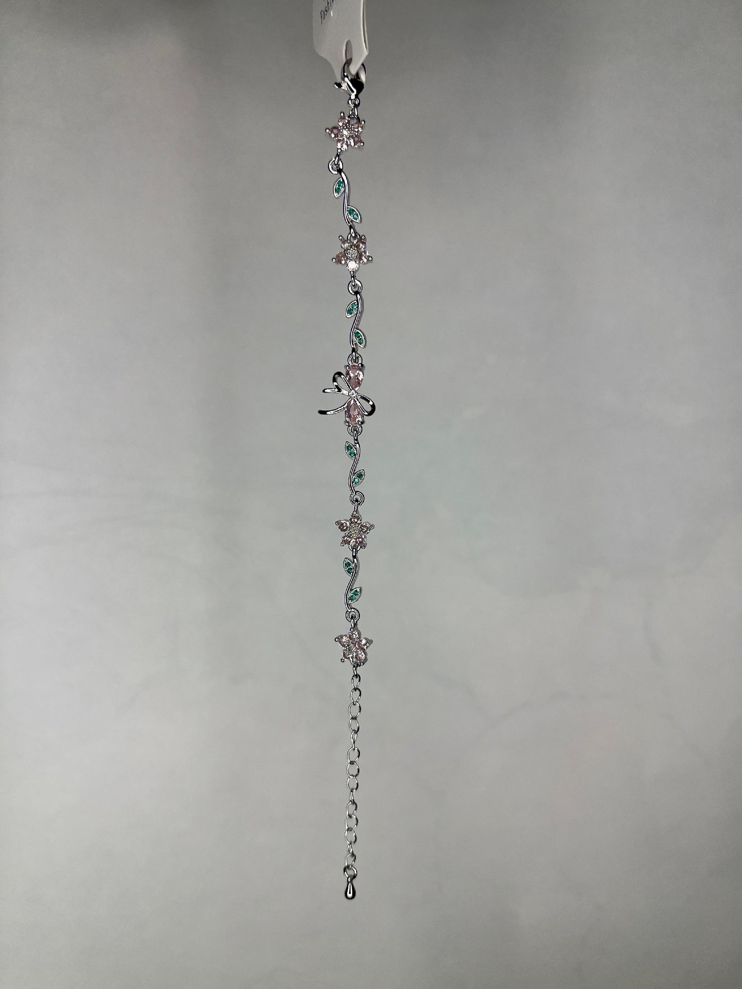 Close-up view of silver floral and dragonfly bracelet showing detailed pink and green crystal adornments on a plain background