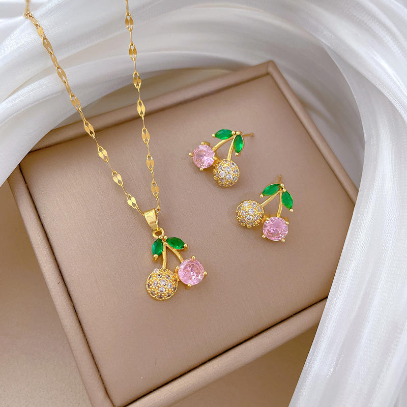 Gold-tone cherry necklace and earrings set displayed on beige background with white fabric