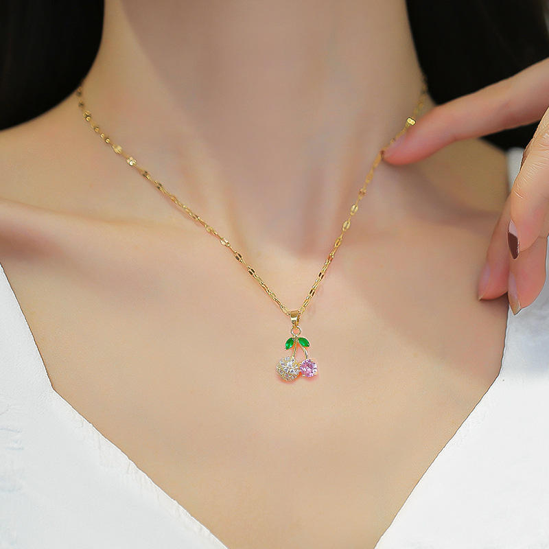 Model wearing gold-tone cherry pendant necklace with pink and clear crystals and green leaf accents